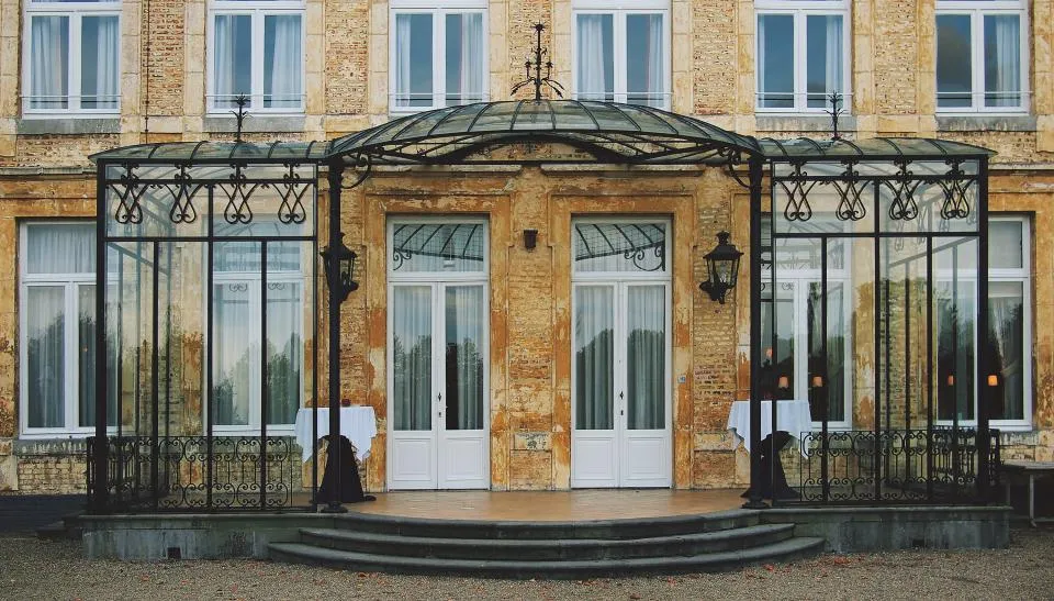 Fachada de château francés de piedra clara con una veranda acristalada de hierro forjado