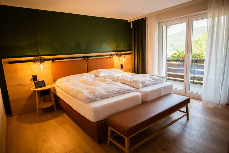 Gemütliches, gut beleuchtetes Hotelzimmer mit Doppelbett und Balkon mit Blick auf die Berge