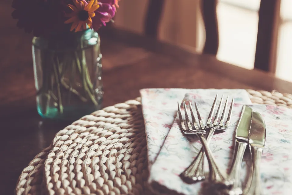 Gedeckter Tisch mit Blumen, Platzset aus Naturfaser und Besteck in warmer Atmosphäre