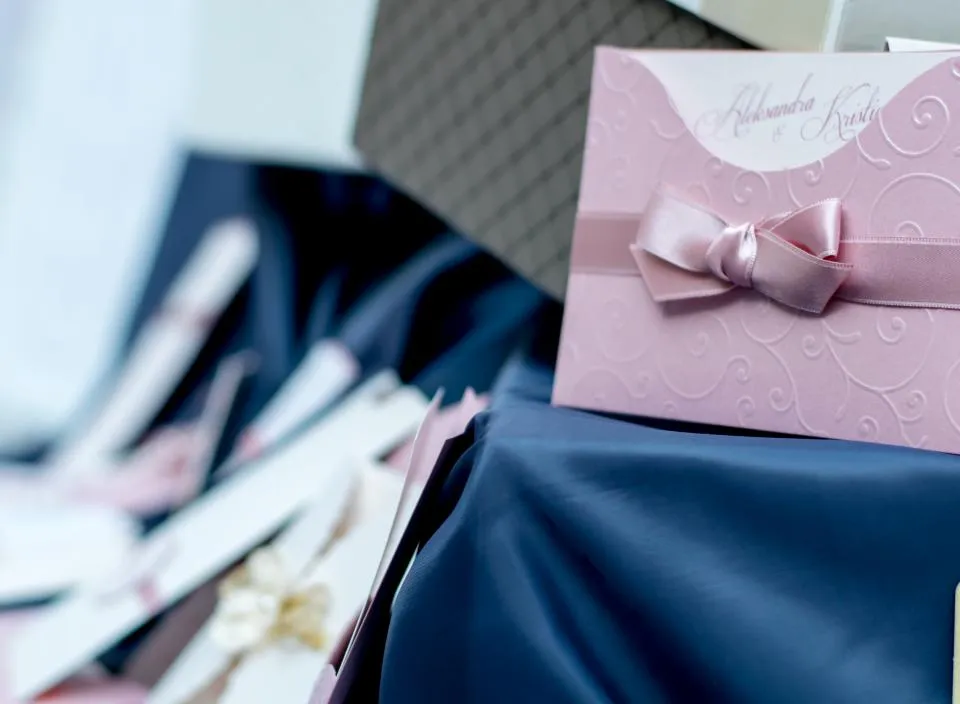 Gedruckte Hochzeitseinladungen neben einem rosa Umschlag mit Schleife