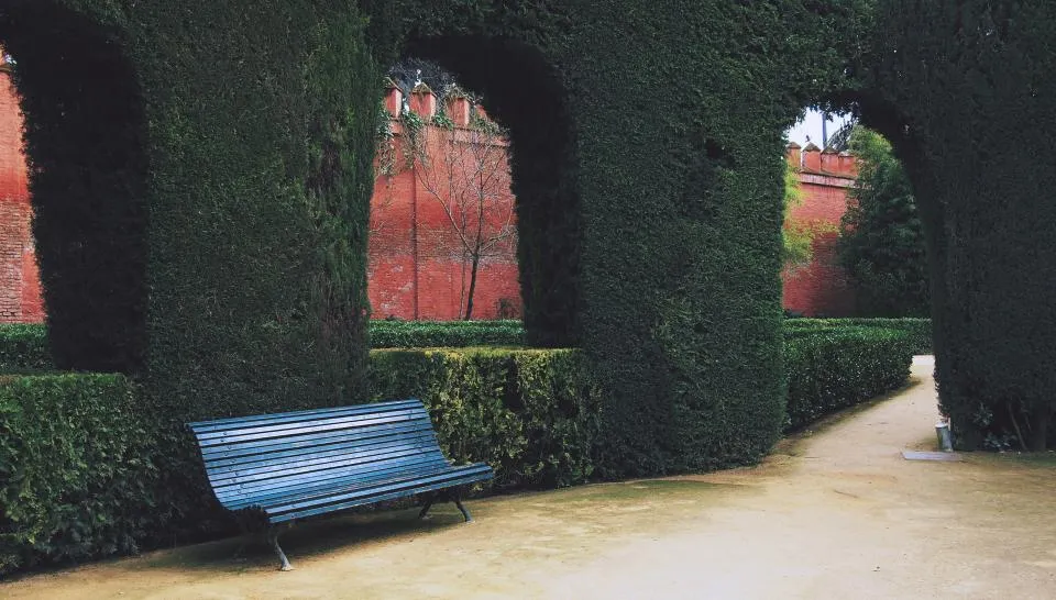 Jardín de setos de ciprés recortados en arcos frente a un muro encalado en tono ocre
