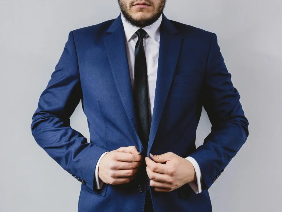 Mann schließt die Jacke eines blauen Anzugs mit Krawatte