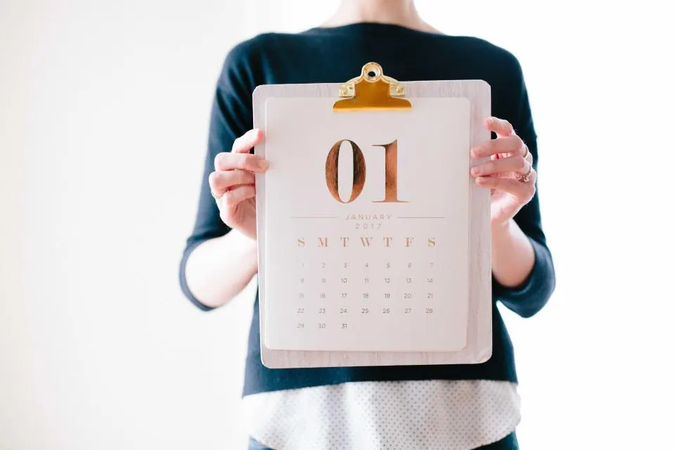 Eine Frau hält ein Holzbrett mit einem minimalistisch gestalteten Monatskalender