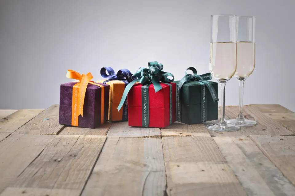 Vier kleine Geschenkschachteln aus Samt mit Satinschleifen neben zwei Sektgläsern