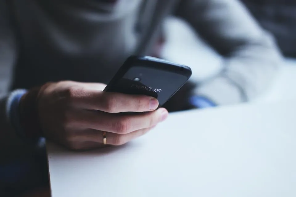 Hand mit Ehering hält ein Smartphone, bereit zum Versenden der Hochzeitseinladung