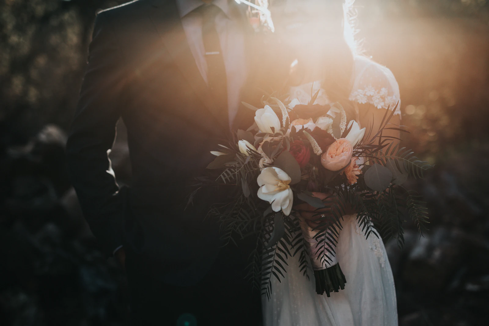 Pareja de recién casados abrazados al atardecer, ella con ramo de flores